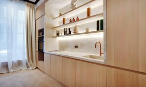 Una cocina moderna con armarios de madera, horno empotrado y un amplio ventanal con cortinas traslúcidas.