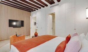 Un dormitorio moderno con una cama grande, un televisor de pantalla plana montado en la pared y un techo de madera.