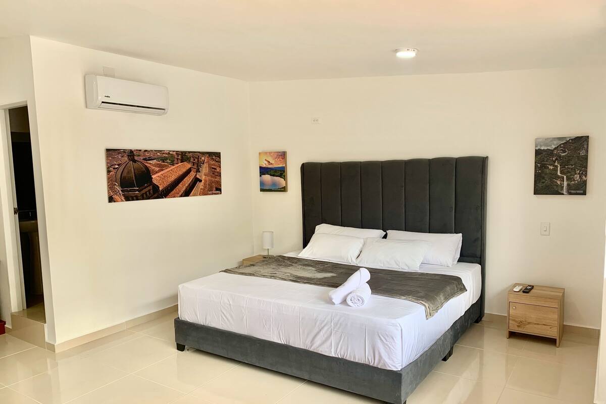 A neatly arranged bedroom with a bed, a bedside table, a nightstand, and wall-mounted air conditioning.