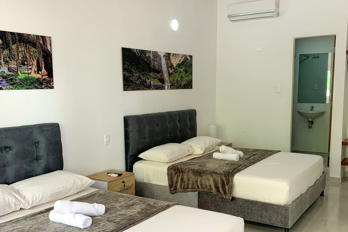 A hotel room with two beds, a bedside table, a mirror, and a wall-mounted air conditioner.