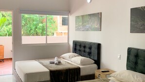 Una habitación de hotel con dos camas, un ventanal amplio, un cuadro y un control remoto en la mesita de noche.