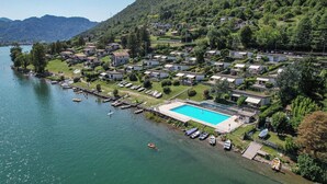 Un complejo turístico junto al lago con piscina, barcos amarrados y casas en la colina.