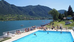 Una piscina con gente, vista a un lago y montañas al fondo.