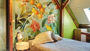 Et soveværelse med et mural af tropisk frugt og blomster på væggen, en seng med puder og et natbord med en lampe.
