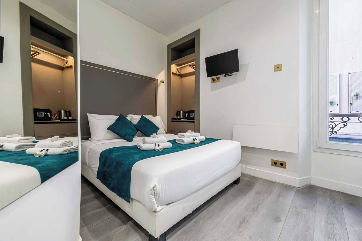 Una camera d'albergo moderna con un letto grande, una TV a schermo piatto fissata al muro e un balcone con vista.