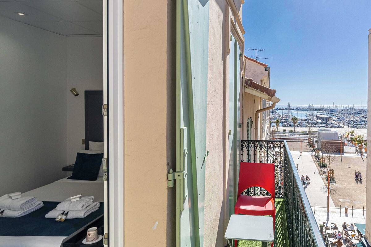 Un balcone con un letto, una sedia rossa e vista su una marina piena di barche.