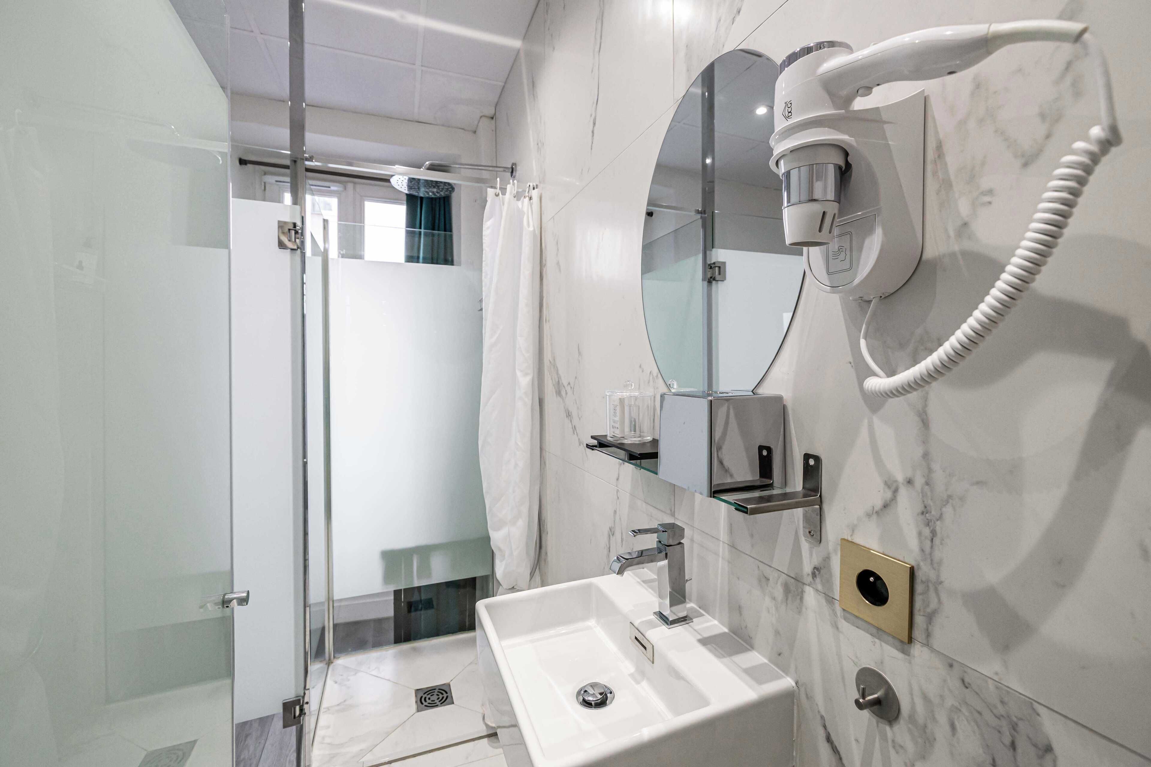 Un baño moderno con cabina de ducha de vidrio, un lavabo blanco y un secador de pelo incorporado.