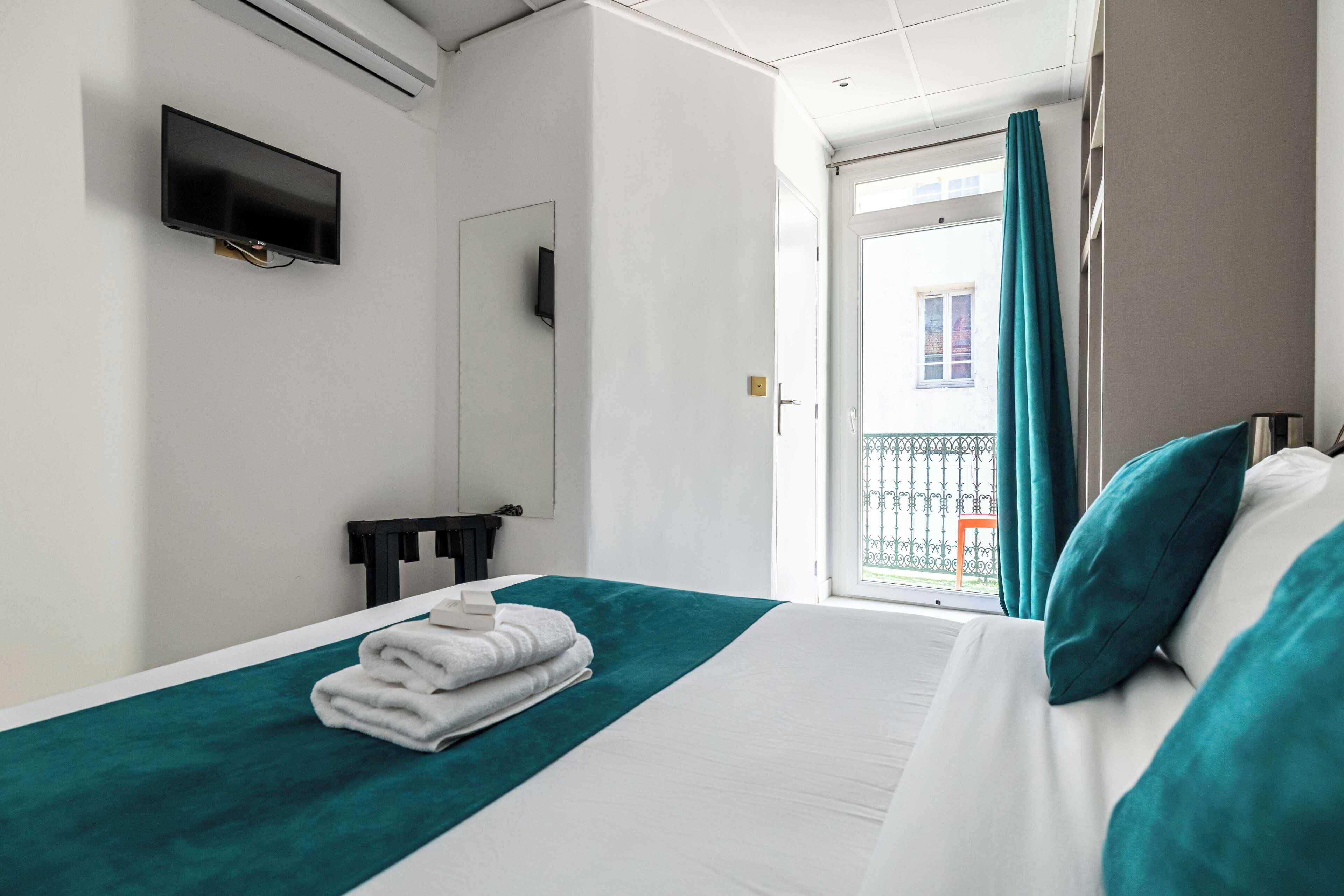 Ein Hotelzimmer mit Bett, Wandfernseher, einem Fenster mit Vorhängen und Blick auf den Außenbalkon.