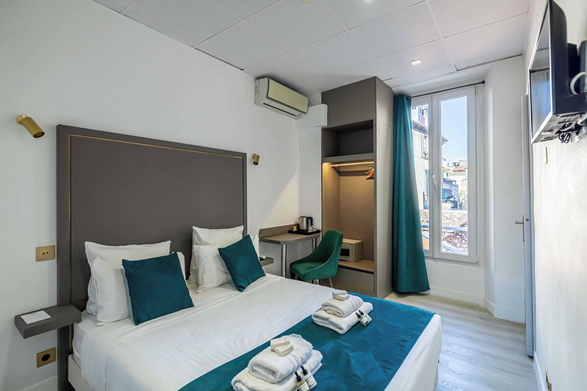 Una camera d'albergo con un letto, una scrivania, una sedia e un condizionatore d'aria.