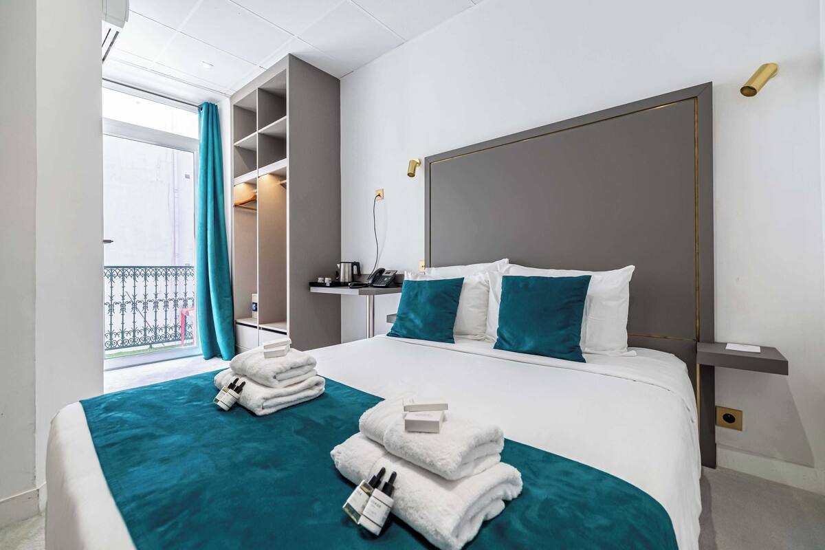 Una camera d'albergo con un letto grande, un comodino, tende a una finestra e vista sul balcone esterno.