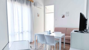 A modern, well-lit room with a dining table and chairs, a sofa, and a television on a stand. - Holiday apartment near the sea (Jesolo)