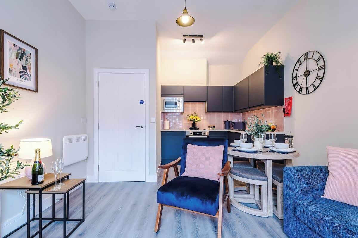A modern kitchen with dark cabinets, a dining area with a blue sofa, and a small table with a bottle of champagne.