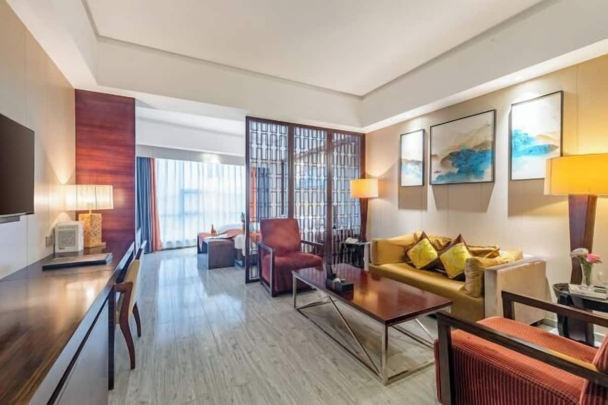 A hotel room with a sofa, armchairs, a coffee table, a TV, and artwork on the walls.