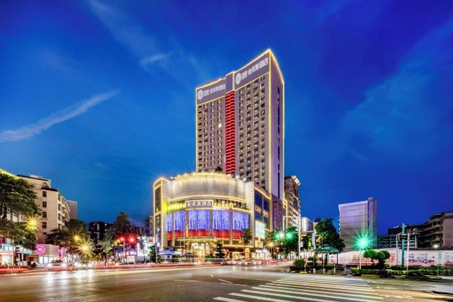 Un hotel moderno de gran altura con un diseño vertical llamativo, varias plantas y una entrada amplia e iluminada.