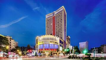 Un hotel moderno de gran altura con un diseño vertical llamativo, varias plantas y una entrada amplia e iluminada.
