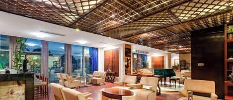 A spacious lobby with a high ceiling, comfortable seating, a reception desk, and a view of the outdoors.