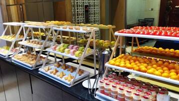 A buffet with multiple trays of pastries, fruits, and beverages.