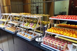 Un bufé con varias bandejas de pasteles, frutas y bebidas.