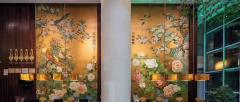 Un espace d’accueil doté d’une grande colonne, d’une décoration murale florale et d’un coin salon avec des fauteuils.