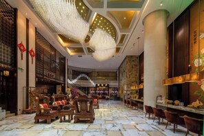 En hotellobby med et marmorgulv, møbler i træ og en stor lysekrone.