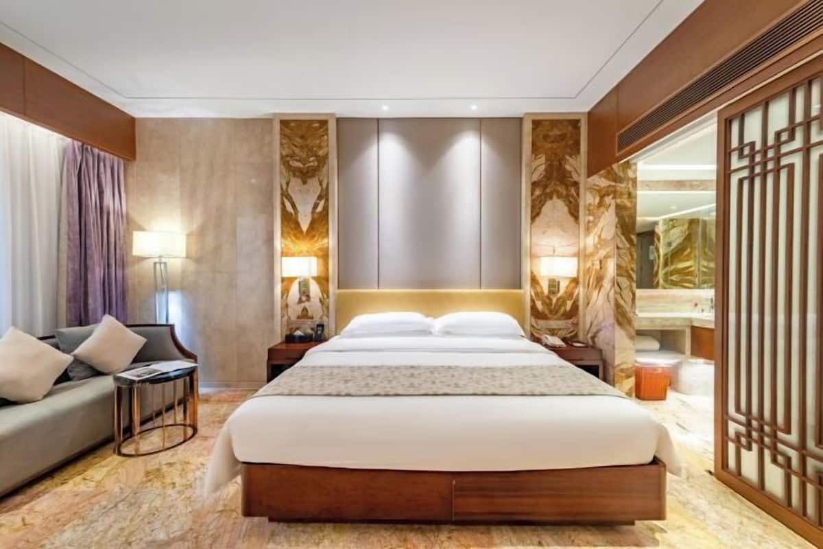 A hotel room with a large bed, a sofa, a nightstand, and a decorative wall panel.