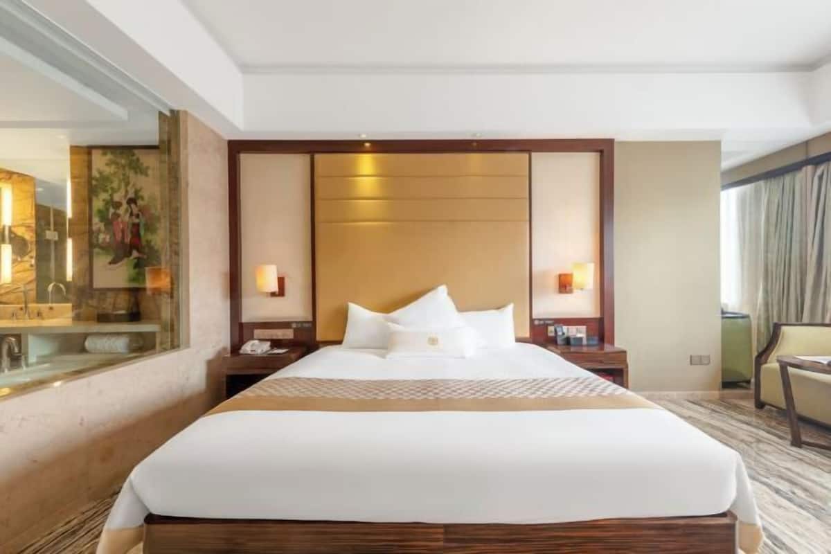 A hotel room with a large bed, a nightstand, a bedside table, and a mirror.