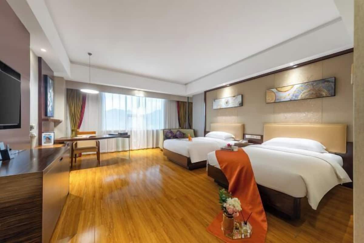 A hotel room with a wooden floor, two beds, a desk, a chair, and a TV.