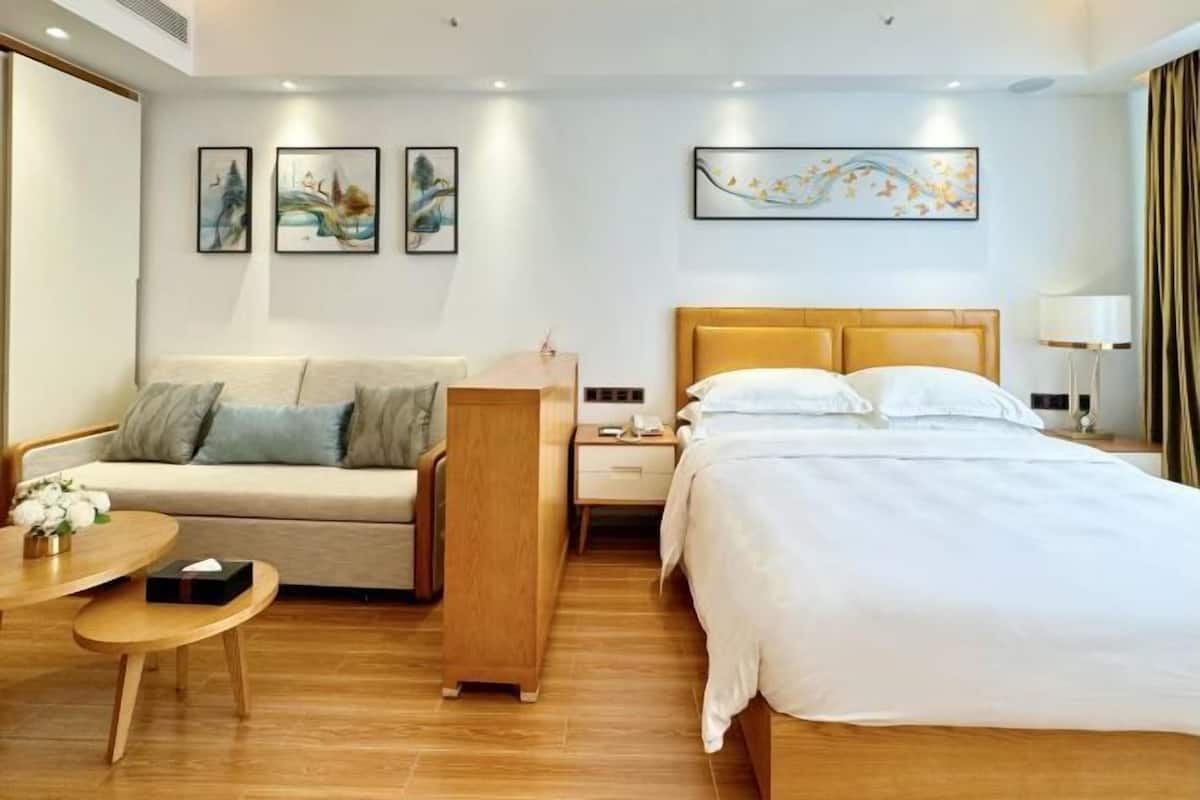 A hotel room with a bed, a sofa, a nightstand, a table, and artwork on the walls.