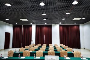 Une salle de conférence avec des rangées de tables, des chaises et une scène avec des rideaux.