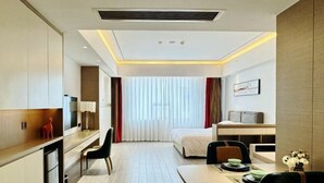 A modern hotel room with a bed, a desk, a chair, a small table, and a TV. - Floral Hotel · YunFu City King Royal Hotel (Yunfu)