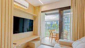 Un salon moderne doté d’un téléviseur à écran plat, d’étagères en bois, d’un canapé et d’une porte-fenêtre coulissante donnant sur un espace repas extérieur.