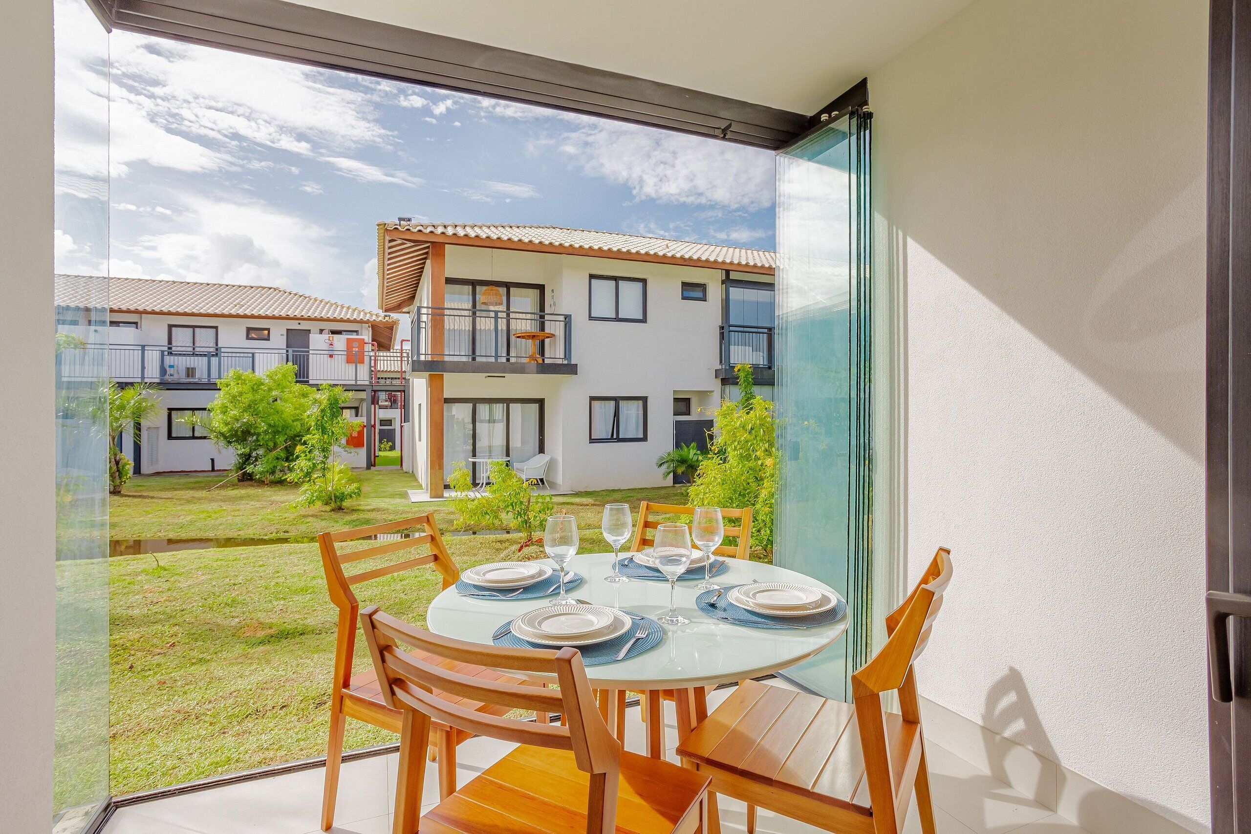 A dining area with a table set for four, overlooking a courtyard with buildings and greenery.