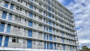 Un edificio de varios pisos con fachada azul y blanca, que incluye balcones y una entrada a nivel de calle.