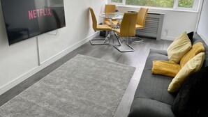 Una sala de estar moderna con un televisor de pantalla plana, un sofá gris, sillas amarillas y una mesa de comedor.