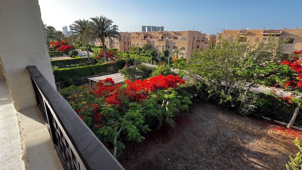 A courtyard with red flowering plants, a paved area, and traditional buildings in the background. - Chalet For Rent In Marina 6 District 31 (North coast)