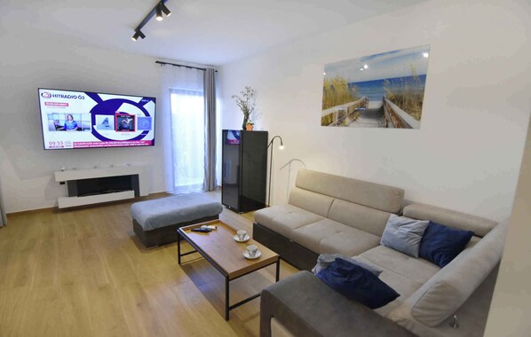 A modern living room with a flat-screen TV, a sofa, a coffee table, and a painting of a beach scene.