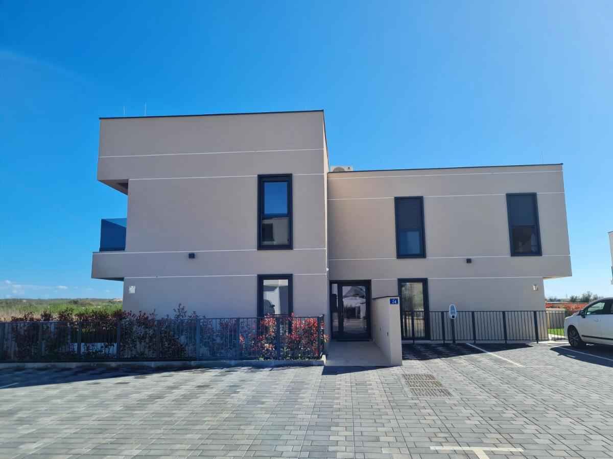 A modern two-story building with a flat roof, large windows, and a paved entrance area.