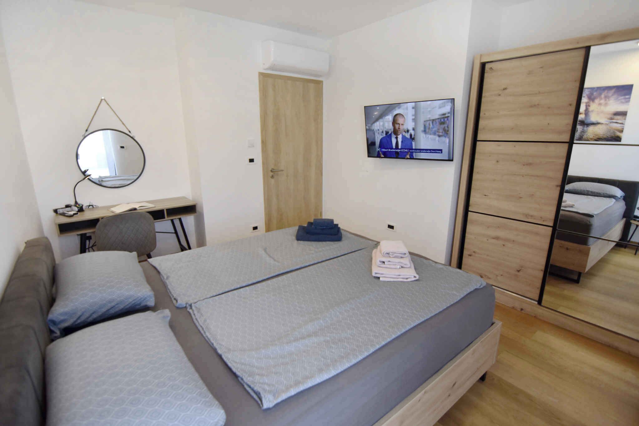A bedroom with two beds, a desk, a chair, a TV, and a wardrobe.