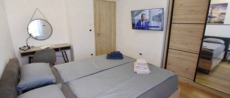 A bedroom with two beds, a desk, a chair, a TV, and a wardrobe.