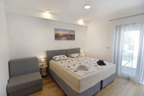 Quarto com cama, sofá, mesa de cabeceira, quadro e janela com cortinas.