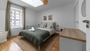 Un dormitorio con tragaluz, cama con cubrecama verde, mesita de noche y cómoda de madera.