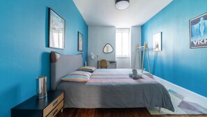 Een slaapkamer met een bed, nachtkastje, stoel, bureau, spiegel en raam.