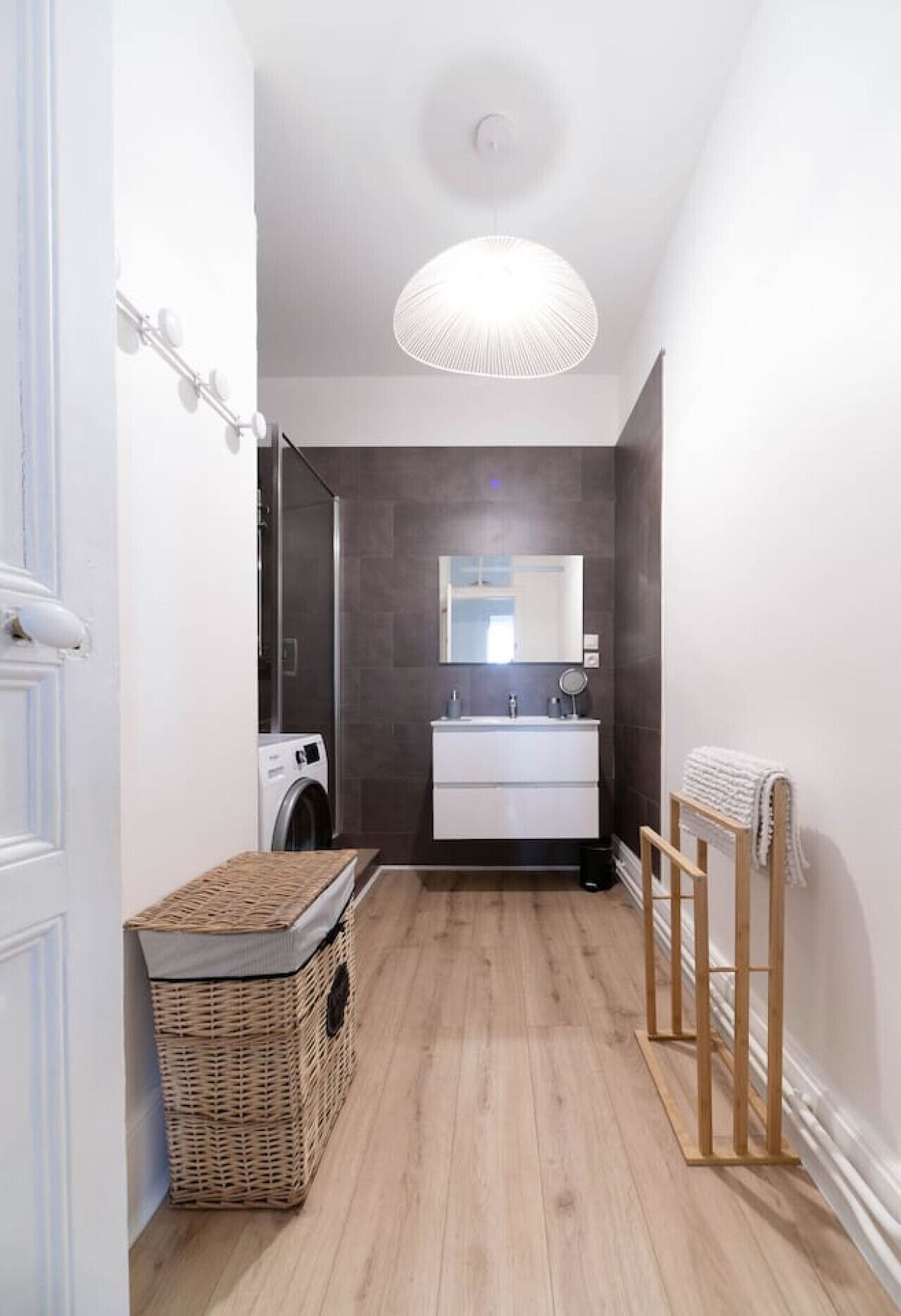 A narrow hallway with a washing machine, a white sink with a mirror, and a wicker basket.
