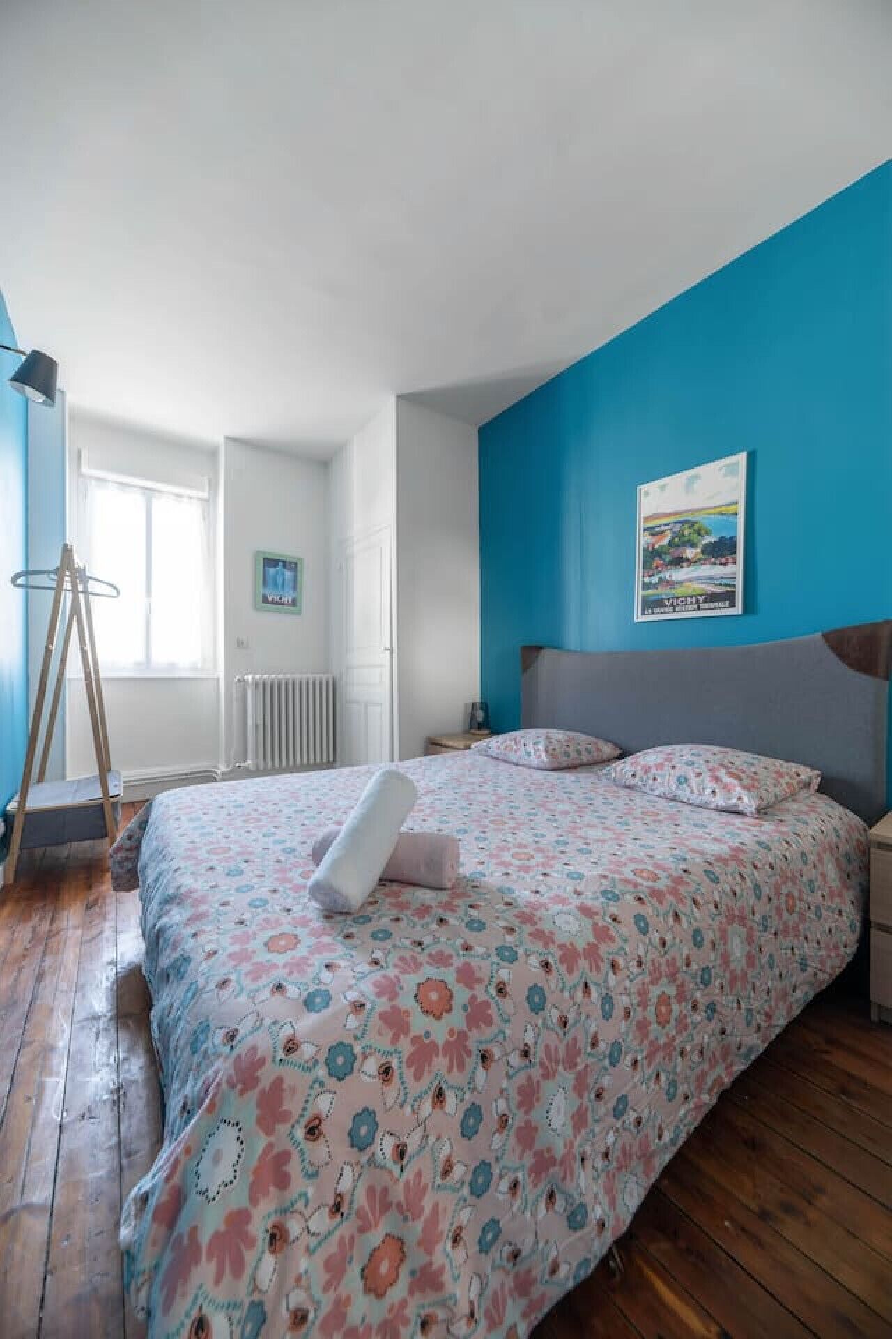 A bedroom with a bed, a nightstand, a window, and a radiator.