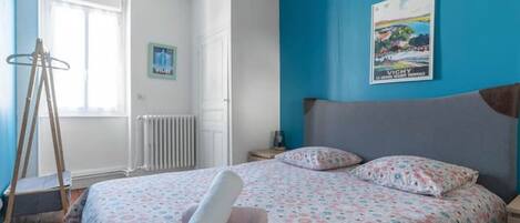 A bedroom with a bed, a nightstand, a window, and a radiator.