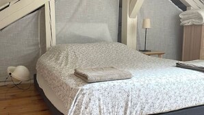 A bedroom with a sloped ceiling, a bed with a floral bedspread, a bedside lamp, and a wooden floor. - Maison calme en plein centre 2 chambres 90m2, Wifi (Clermont-Ferrand)