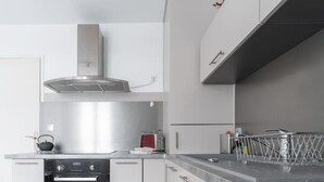 A modern kitchen with white cabinetry, stainless steel appliances, and a tiled floor. - Superbe appartement centre-ville avec terrasse (Vichy)