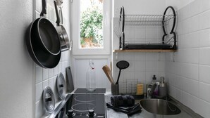 A modern kitchen with a gas stove, hanging pots, a drying rack, and a window with a view of greenery. - Studio design - centre ville - parcs (Vichy)
