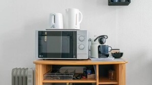 A kitchen area with a microwave, coffee maker, and a small shelf with a kettle and cups. - Studio design - centre ville - parcs (Vichy)