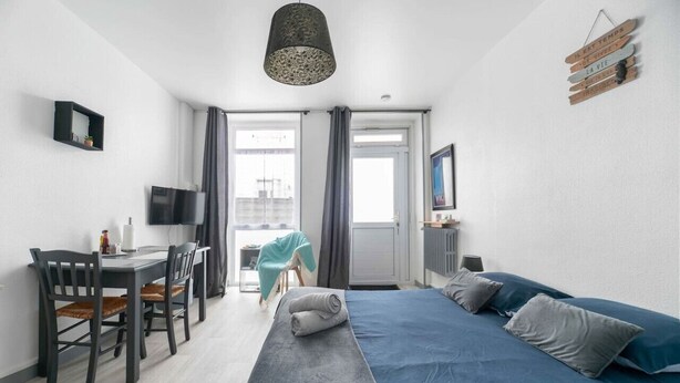 A modern bedroom with a large bed, a desk with a chair, a television, and a window with curtains. - Studio design - centre ville - parcs (Vichy)
